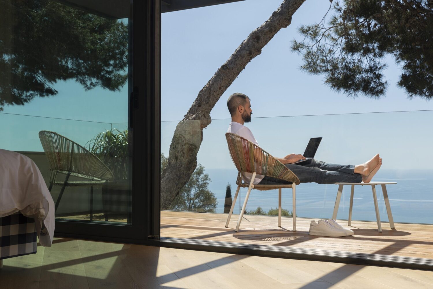 Hombre trabajando con ordenador en una terraza frente al mar, representando teletrabajo internacional y Ley Beckham en España